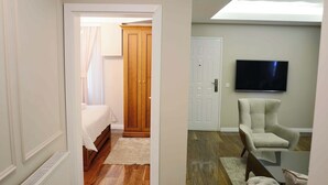 A bedroom with a bed, a wardrobe, a television, and a seating area with a chair and ottoman. - Hotel Begolli (Pristina)