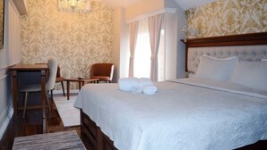A hotel room with a large bed, a desk with a chair, a chandelier, and patterned wallpaper. - Hotel Begolli (Pristina)