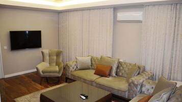 A living room with a flat-screen TV, a tufted sofa, a matching armchair, and a coffee table.