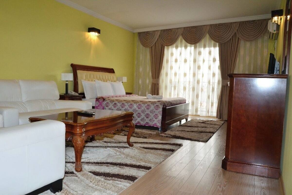 A hotel room with a bed, a sofa, a wooden coffee table, and a desk.