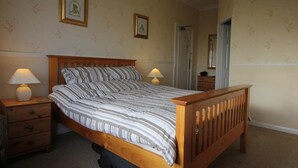 A bedroom with a wooden bed, two bedside tables with lamps, a dresser, and two framed pictures on the wall.