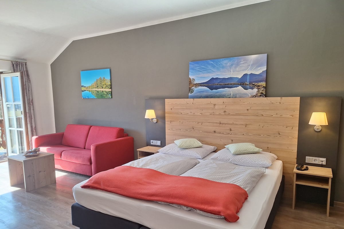A modern hotel room with a large bed, a red armchair, two wall-mounted lamps, and two paintings on the wall.