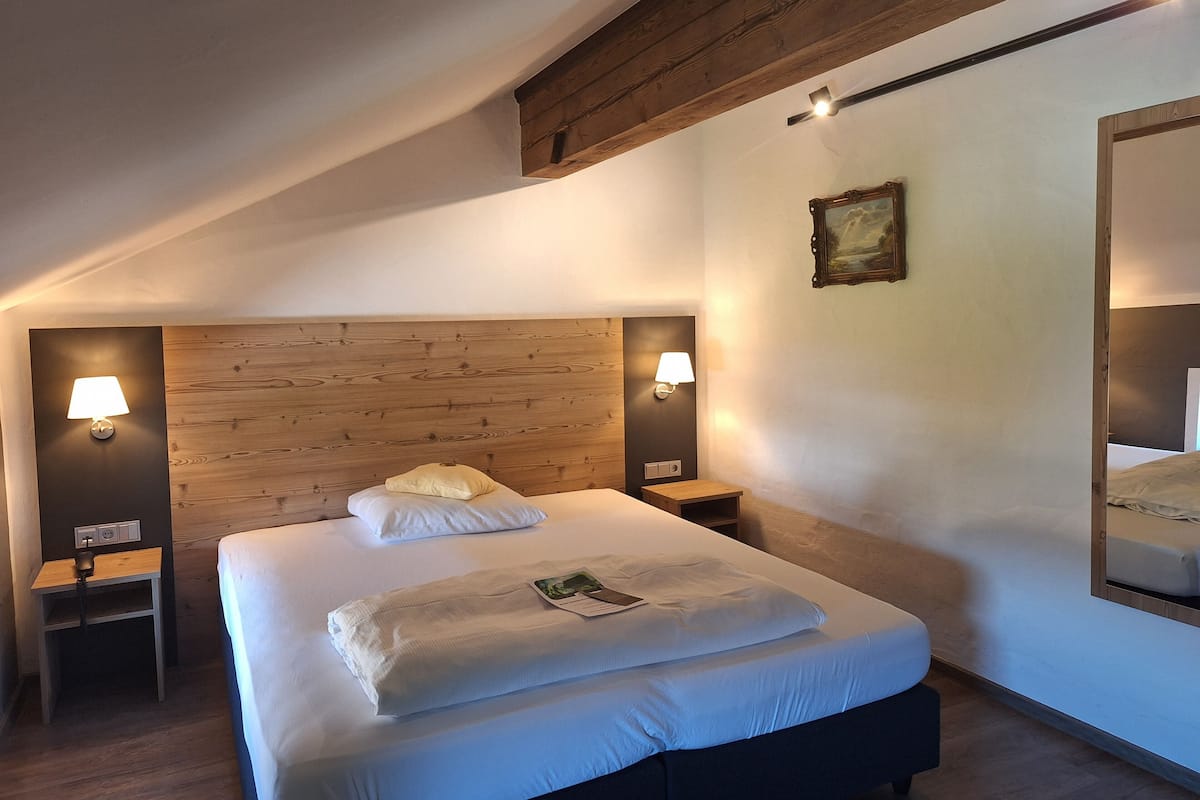 A neatly made bed with pillows and a folded blanket, two bedside lamps, a small table with a lamp, and a painting on the wall.