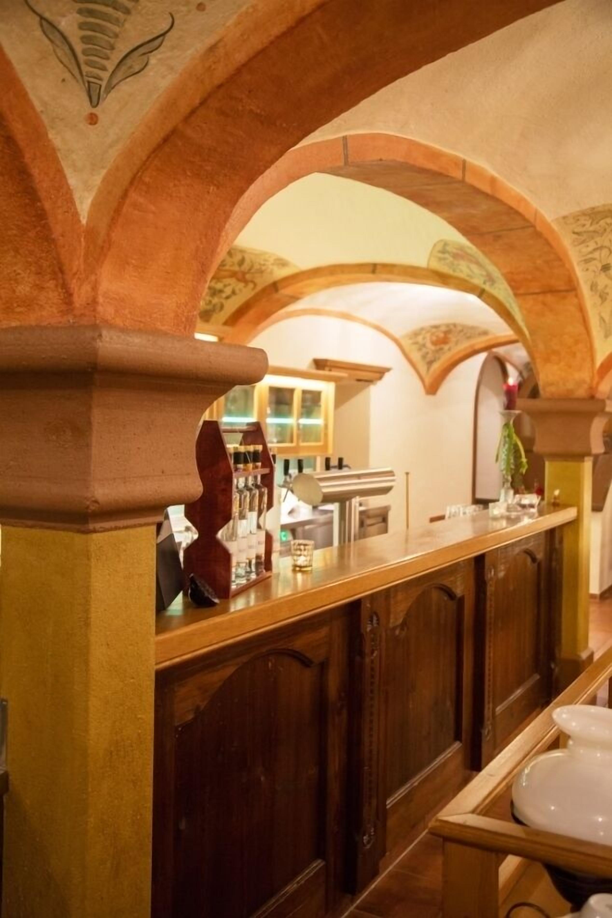 A bar area with a wooden counter, arched ceiling, and a view of the room in the background.