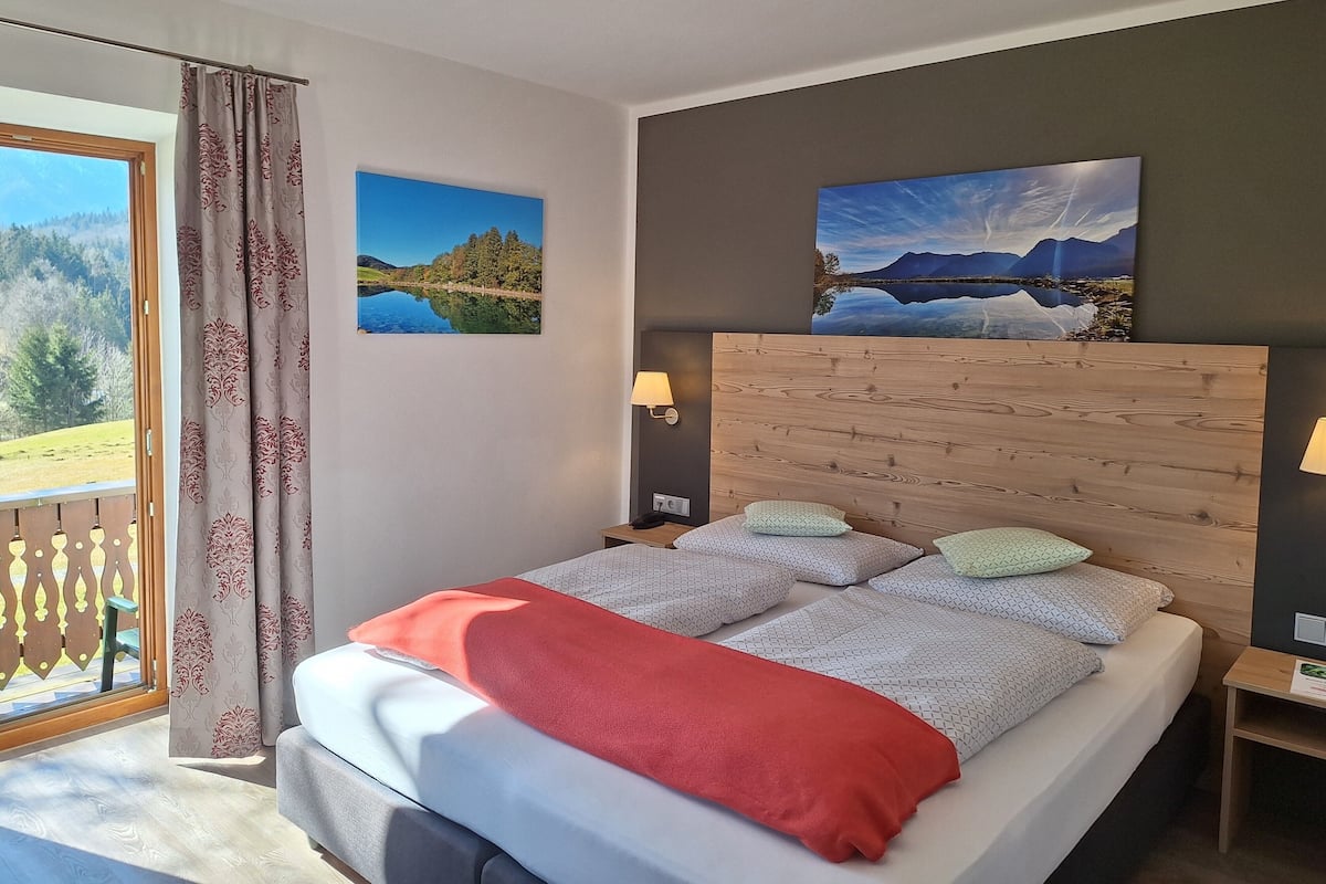 A bedroom with a bed, two wall-mounted lamps, and two landscape paintings.