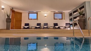 A pool area with lounge chairs, a wooden door, and a view of the sky through windows. - Hotel Heissenhof (Inzell)