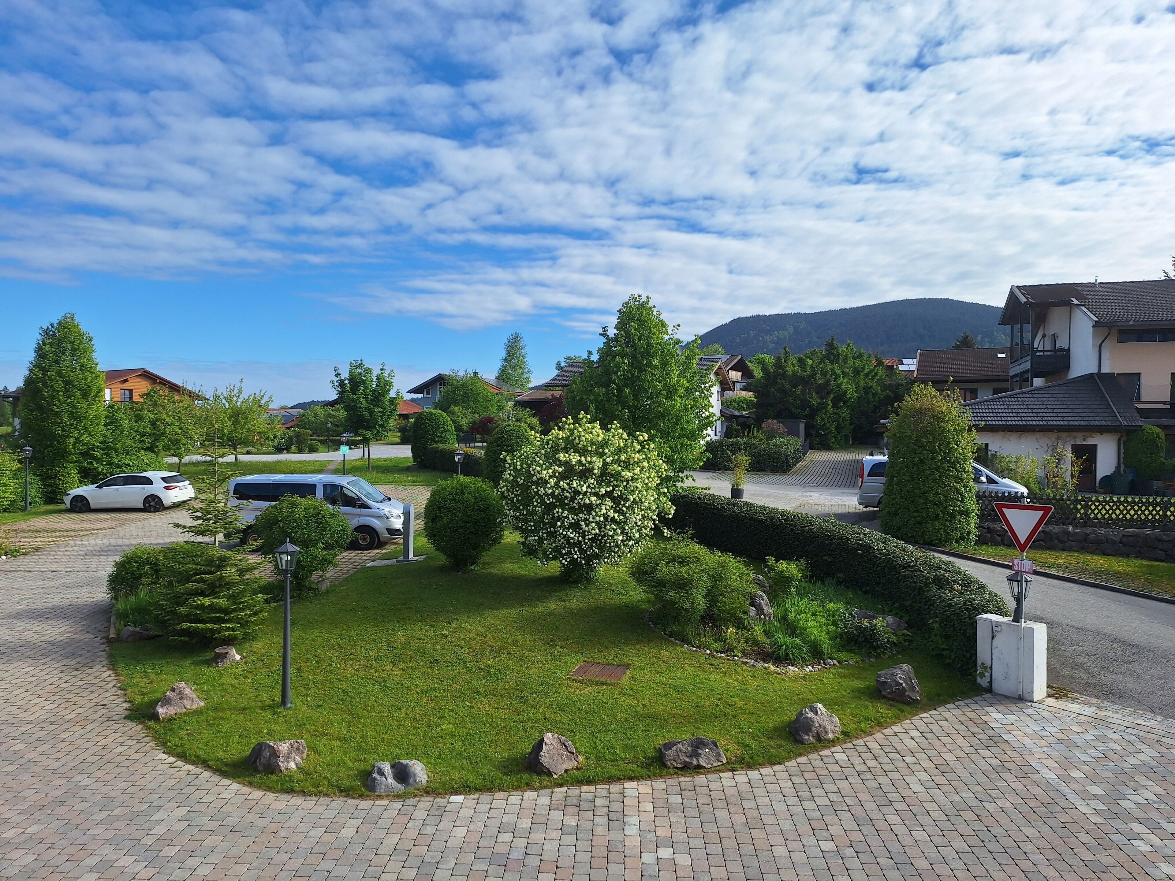 A residential area with houses, parked cars, and a well-maintained lawn with rocks and bushes.