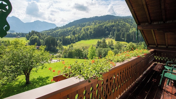 A balcony with a wooden railing overlooking a green valley with trees and mountains in the background. - Hotel Heissenhof (Inzell)