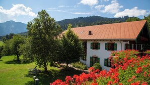 A house with a red-tiled roof, surrounded by lush greenery and red flowers. - Hotel Heissenhof (Inzell)