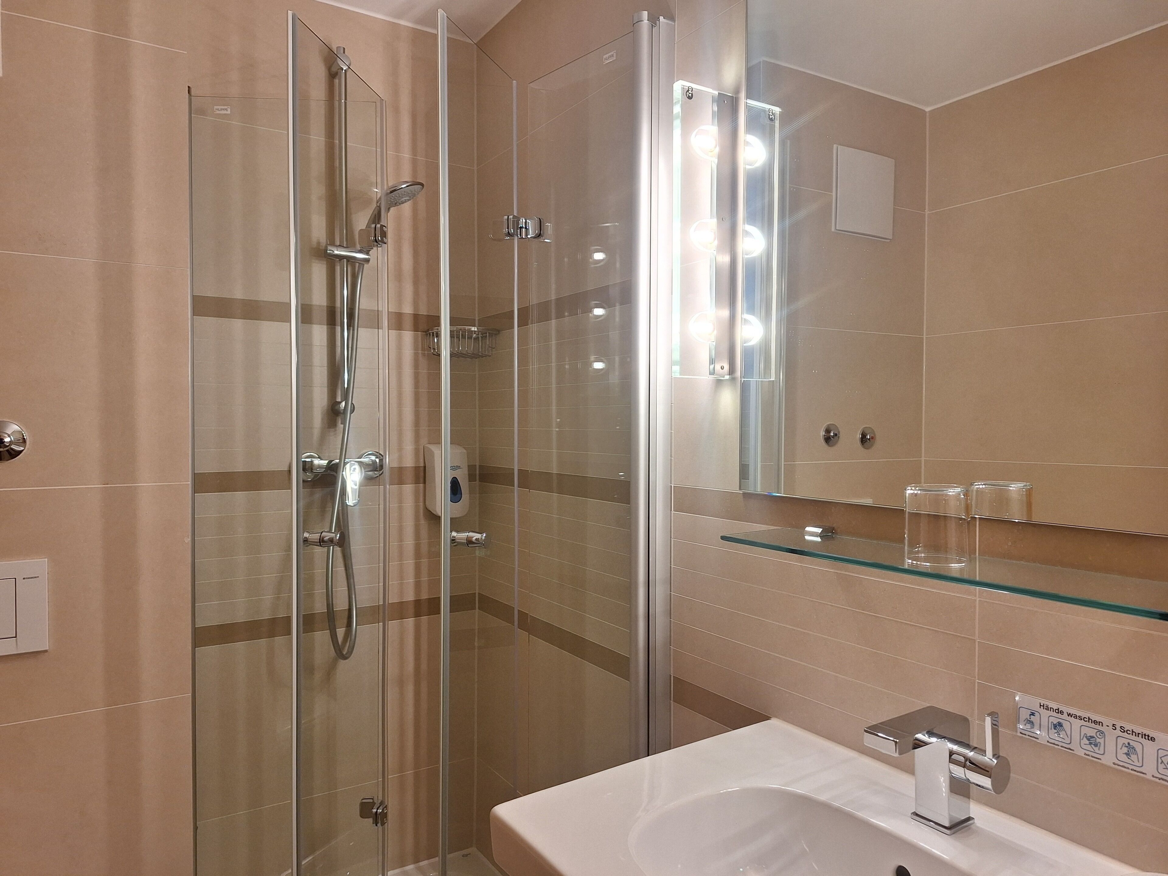A modern bathroom with a glass-enclosed shower, a glass-topped sink, and a mirror with lights.