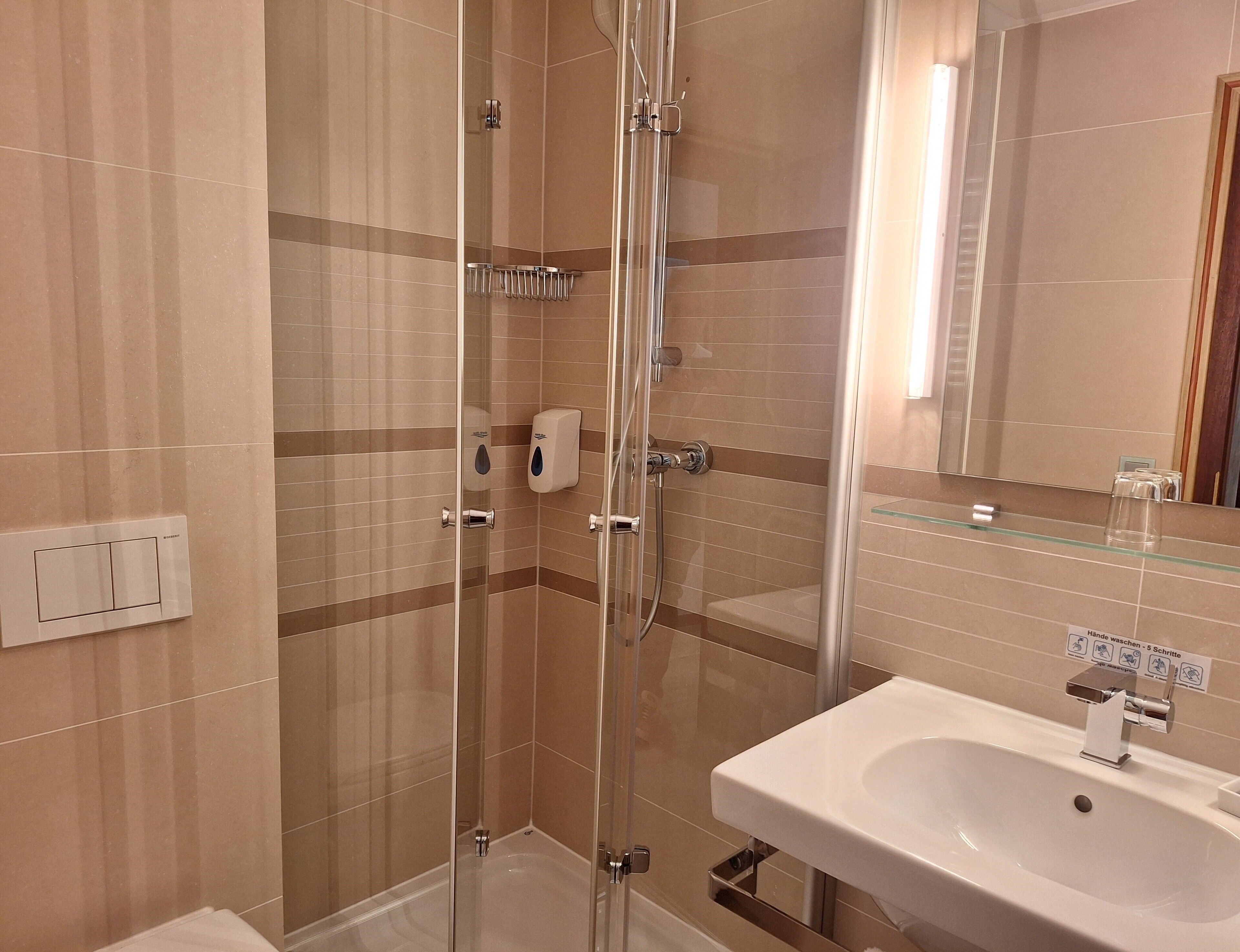 A modern bathroom with a glass-enclosed shower, a white sink, and a mirror.