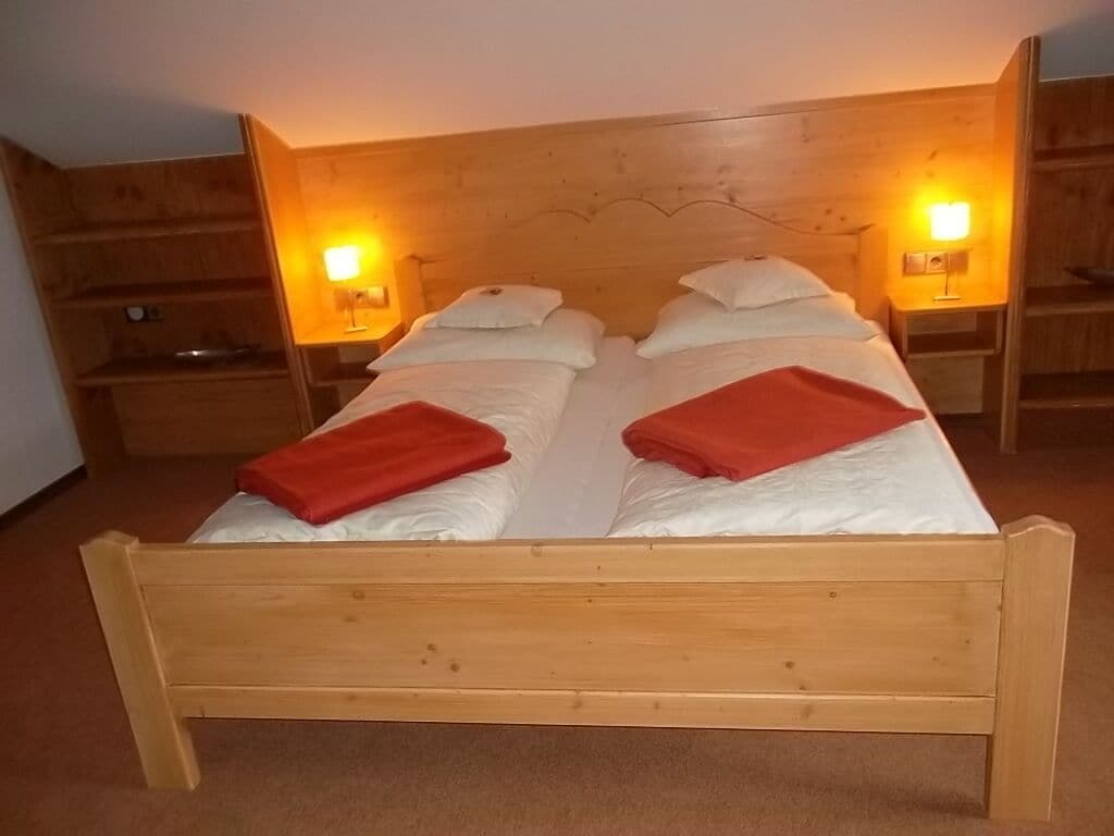 Una cama doble con estructura de madera, dos mesitas de noche con lámparas y un armario de madera.