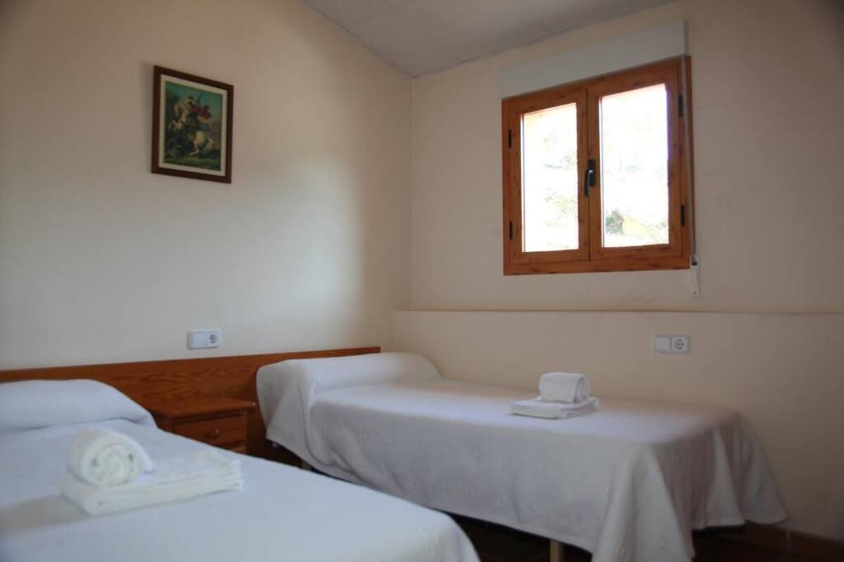 Ein Hotelzimmer mit zwei Einzelbetten, einem Holzkopfstück, einem Fenster mit Holzrahmen und einem Gemälde an der Wand.