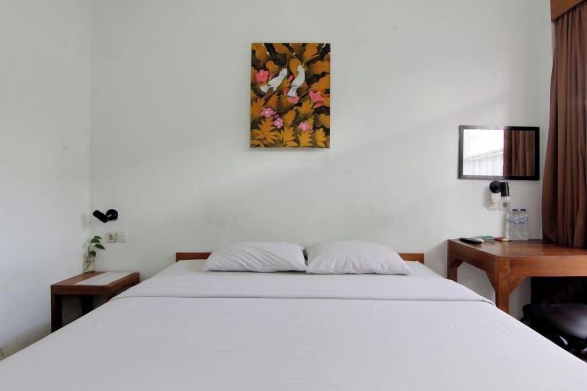 Una habitación de hotel con cama, escritorio, silla, un cuadro en la pared, mesita de noche y lámpara.