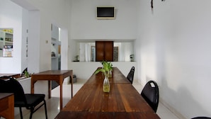 Una larga mesa de madera con sillas, un florero con plantas y un televisor en la pared.