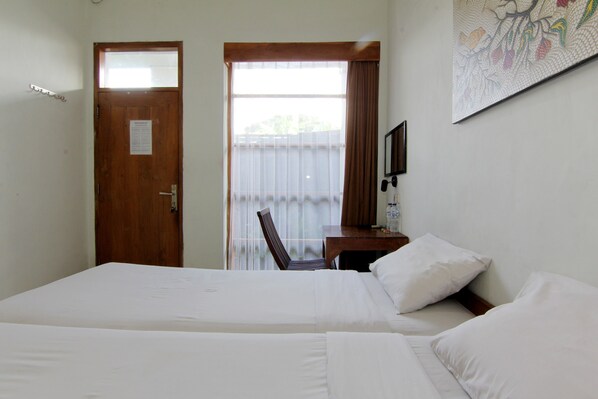 A hotel room with two beds, a desk with a chair, a window with curtains, and a wall-mounted TV.