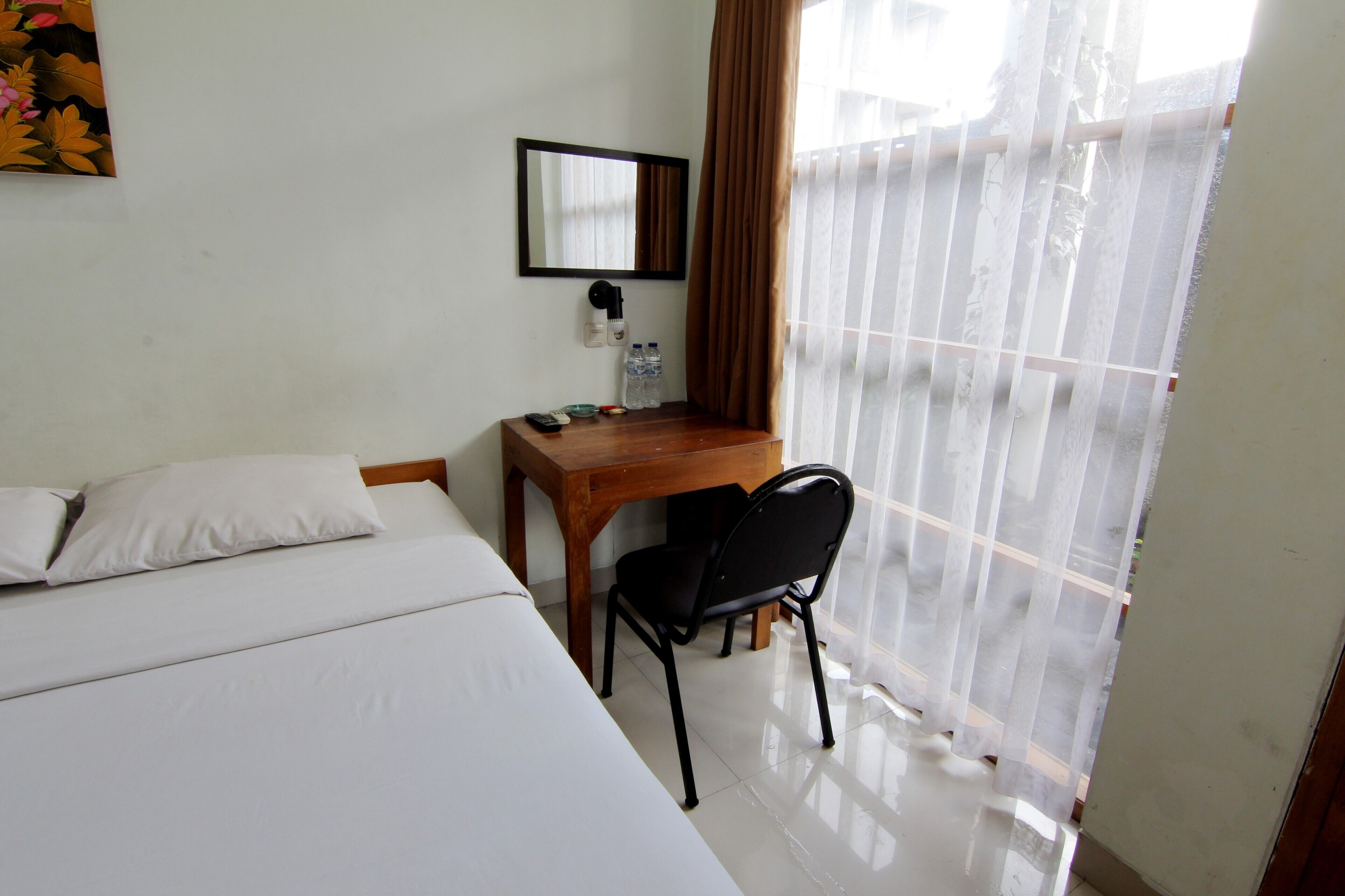 A hotel room with a bed, a desk, a chair, a mirror, and a window with curtains.