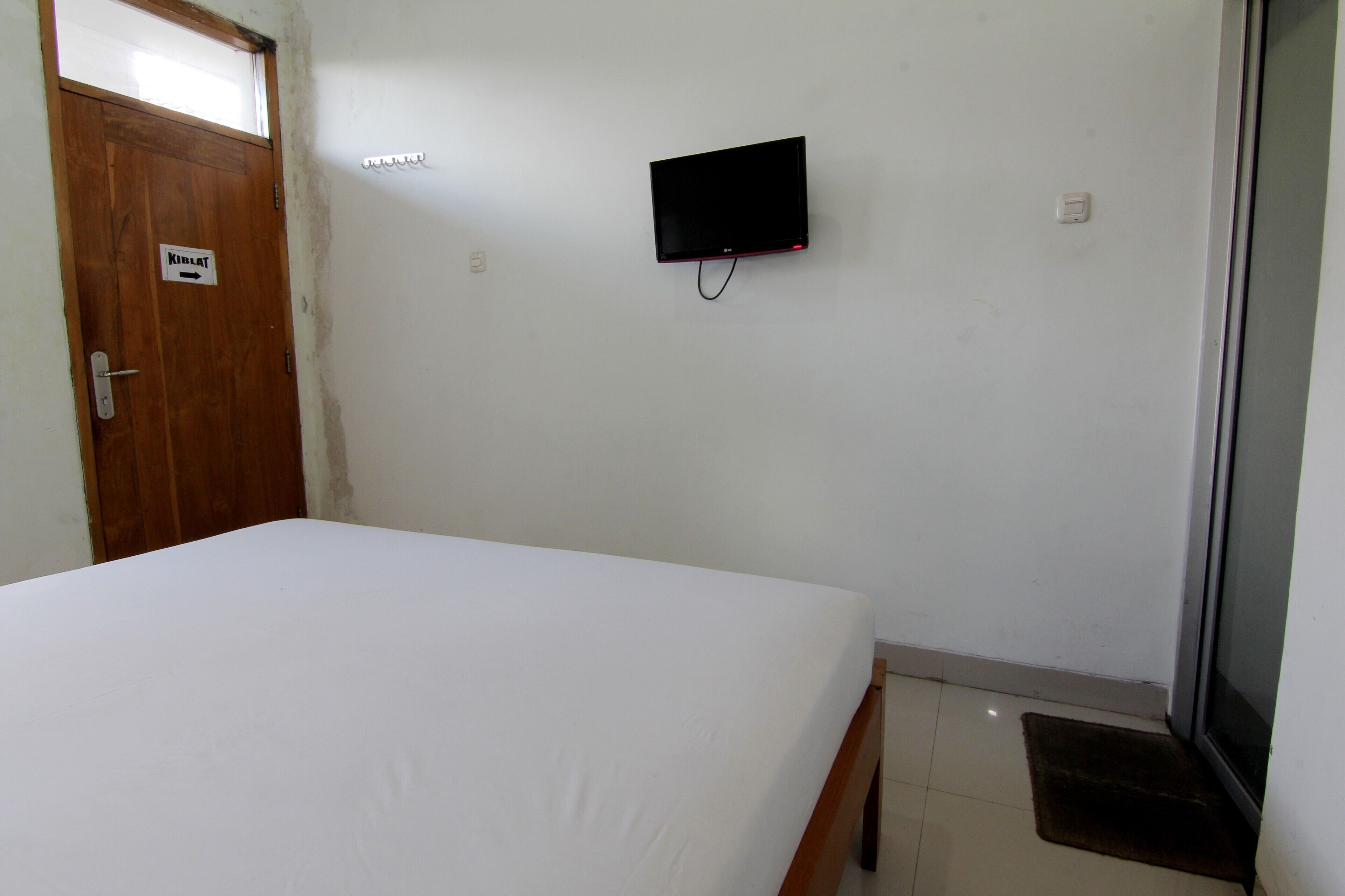 A room with a bed, a television mounted on the wall, a door with a sign, and a small window.