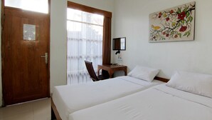 Habitación de hotel con dos camas, una puerta de madera, una ventana con cortinas, una mesita con una silla y un televisor montado en la pared.