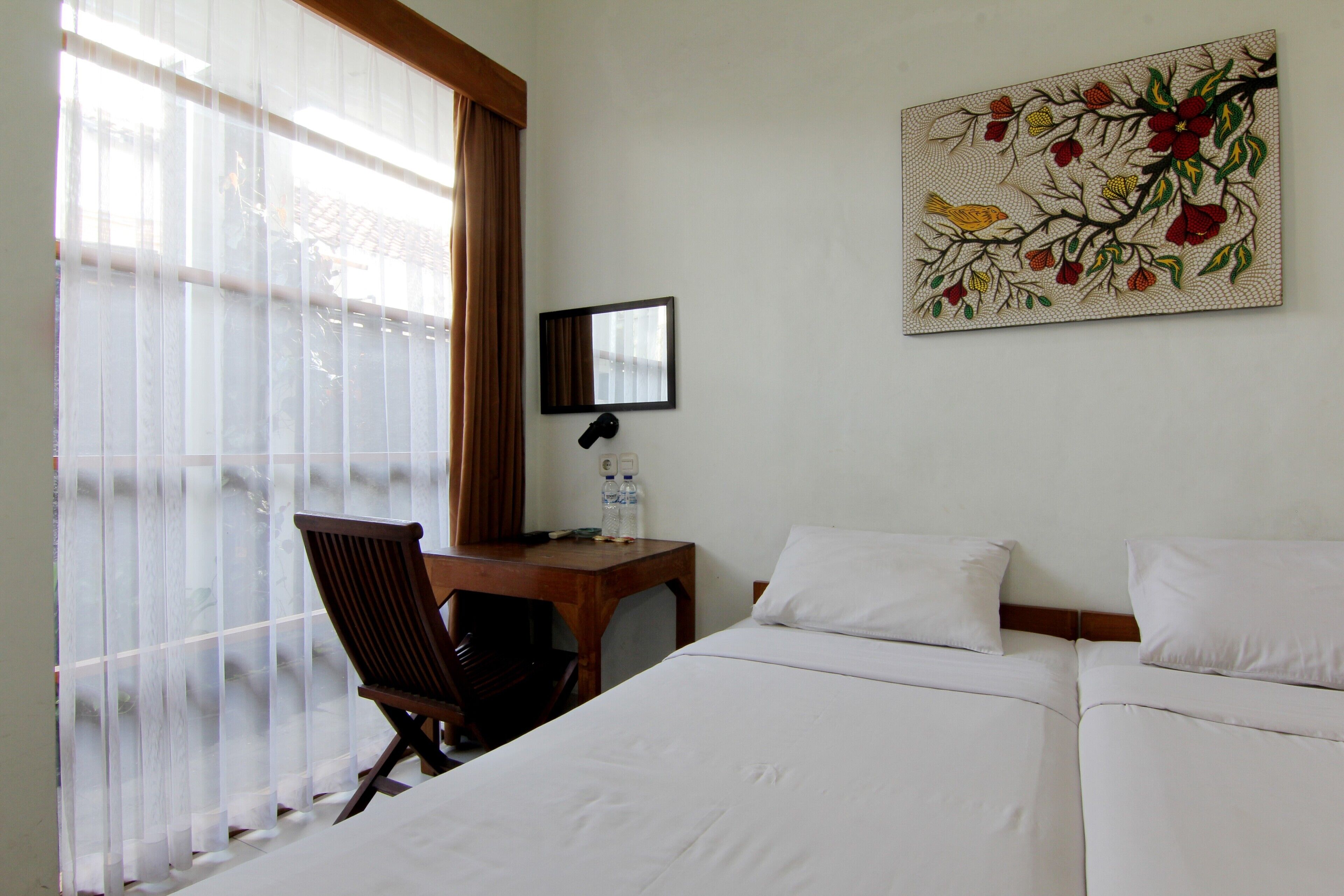 A hotel room with a bed, a desk, a chair, a window with curtains, and a wall-mounted mirror.