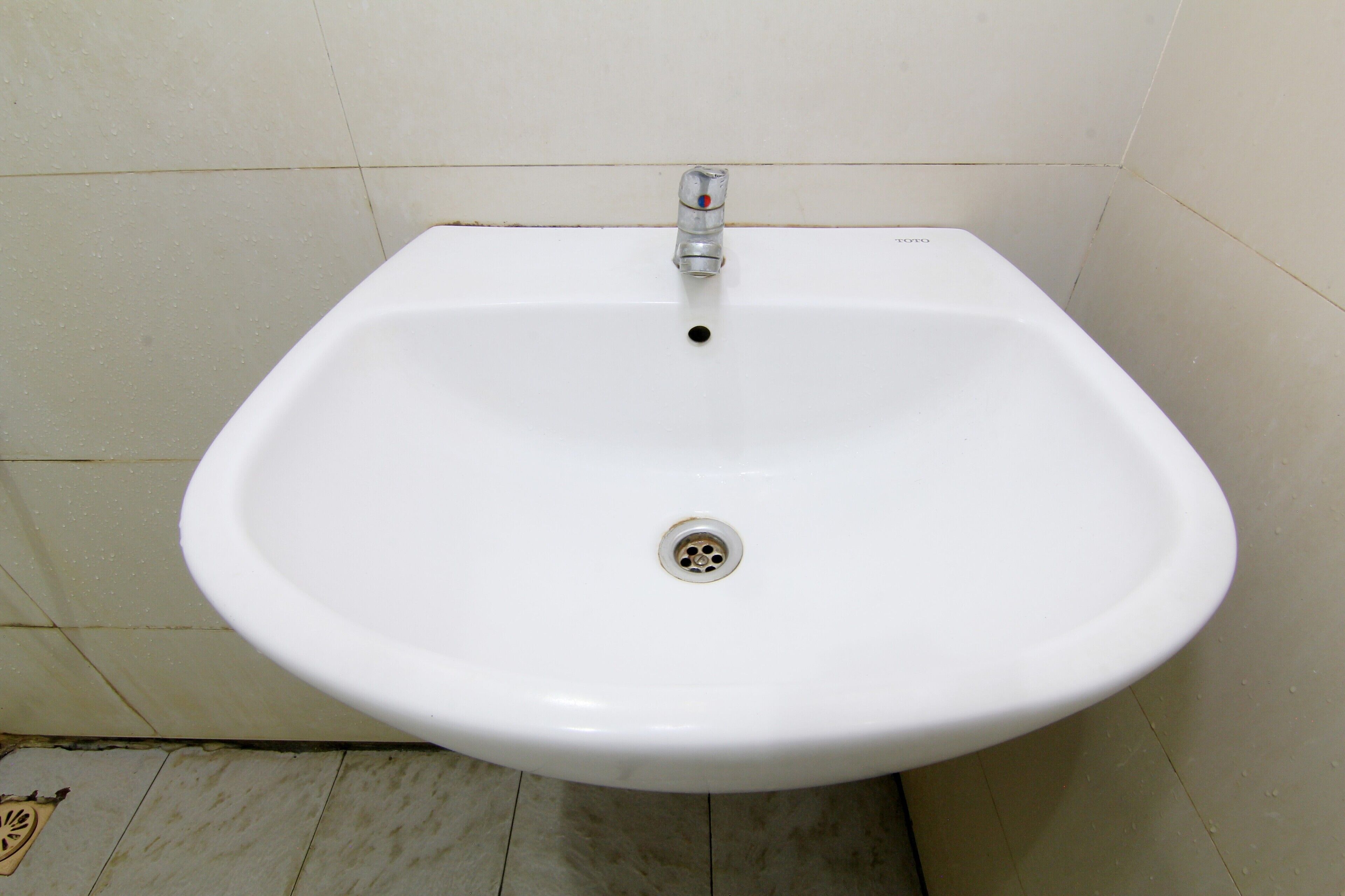 Un lavamanos blanco sobre pedestal con un solo grifo y desagüe en un baño con paredes y suelo de baldosas.
