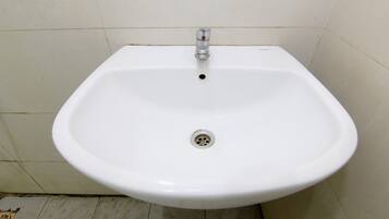 Un lavamanos blanco sobre pedestal con un solo grifo y desagüe en un baño con paredes y suelo de baldosas.