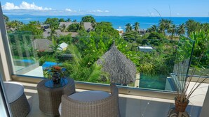 A balcony with wicker furniture, a decorative vase, and a view of the ocean and tropical landscape. - Bel Horizon (Nosy Be)