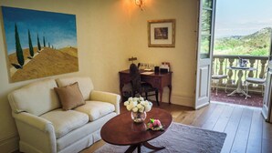 Un salón con un sofá blanco, una mesa de centro de madera con flores, un escritorio con una silla, un cuadro en la pared y vistas a un balcón con mobiliario exterior.