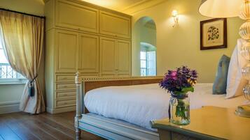 A bedroom with a large bed, a nightstand, a vase with flowers, and a wall-mounted lamp.