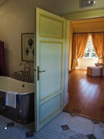 Un baño con bañera, un cuadro en la pared y una puerta que da a una habitación con ventana y cortinas.