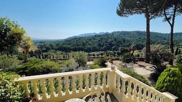 Ein Balkon mit Blick auf einen üppigen Garten und ferne Berge.