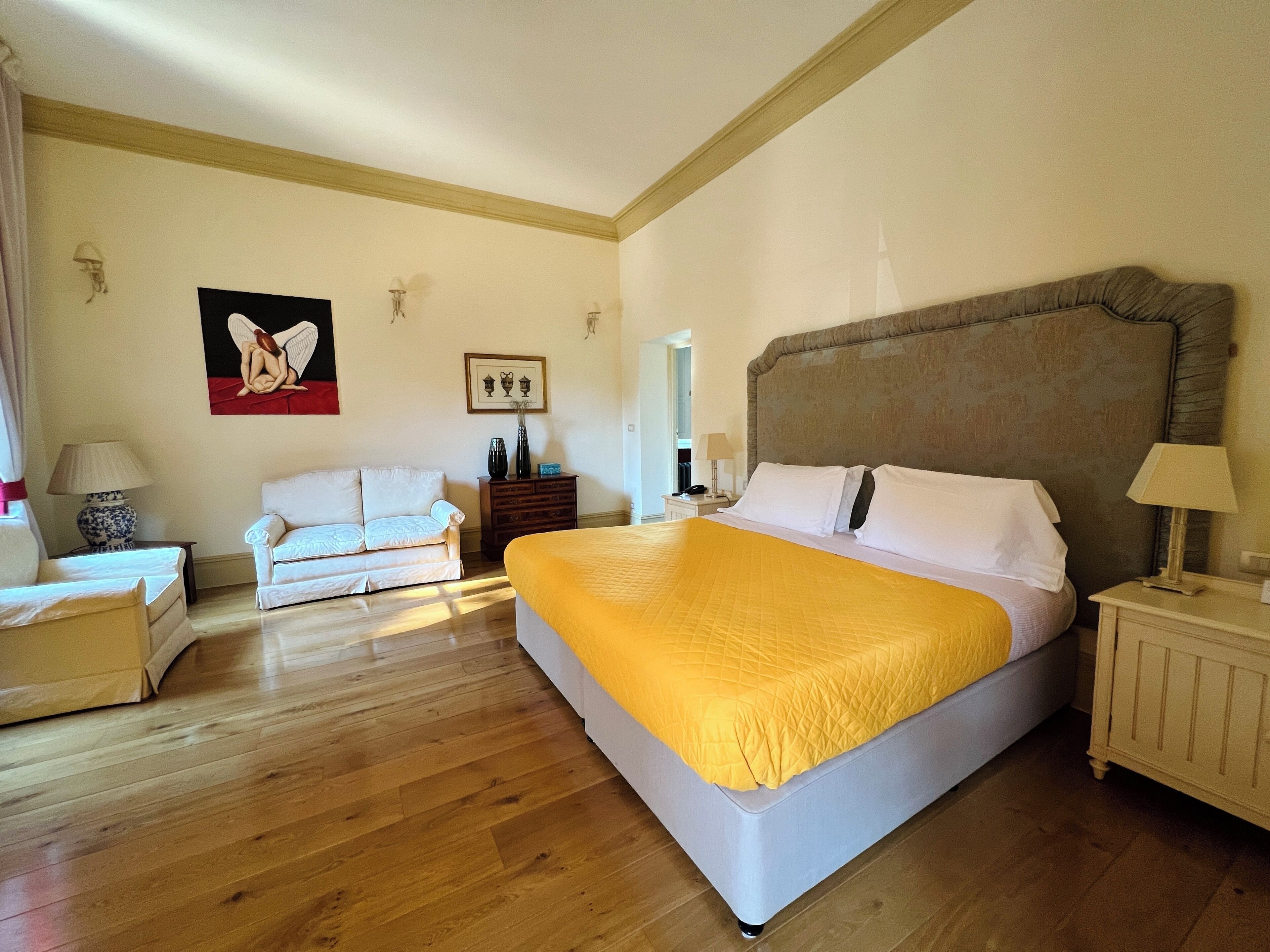 A hotel room with a large bed, a sofa, a dresser, and a painting on the wall.
