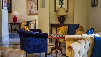 Un salon spacieux avec un jeu d’échecs sur une table ronde, un fauteuil bleu et un canapé jaune agrémenté de coussins bleus.