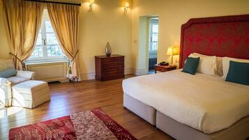 A hotel room with a large bed, a sofa, a wooden dresser, and a red patterned rug.