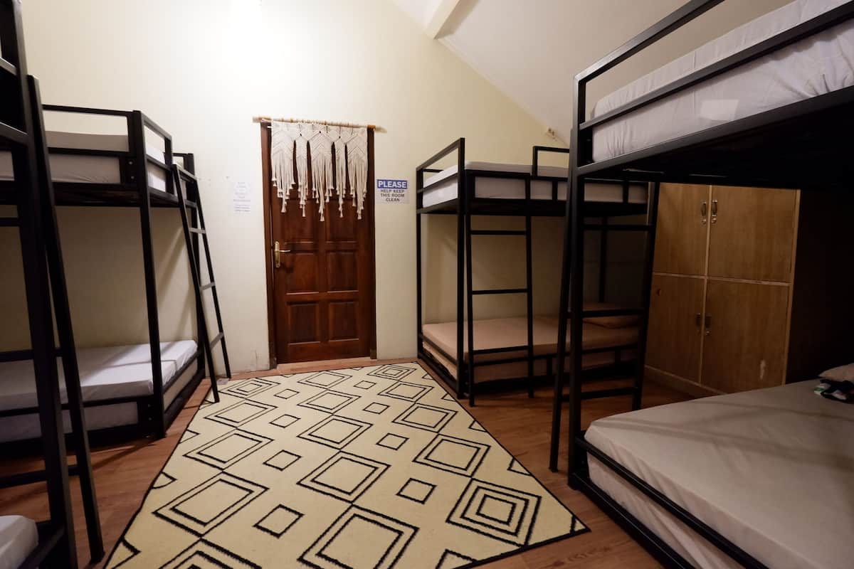 A dormitory room with bunk beds, a wooden wardrobe, and a patterned rug.