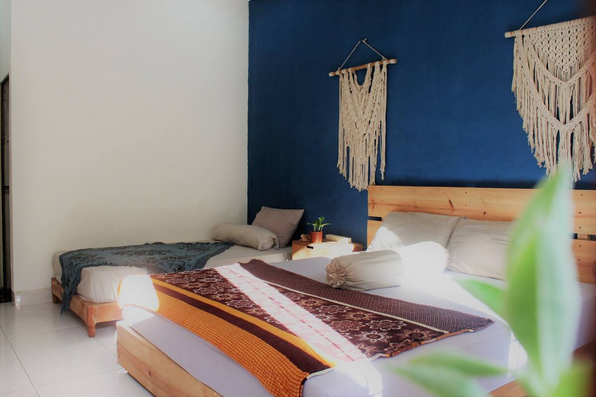 A bedroom with two beds, a macrame wall hanging, and a potted plant.
