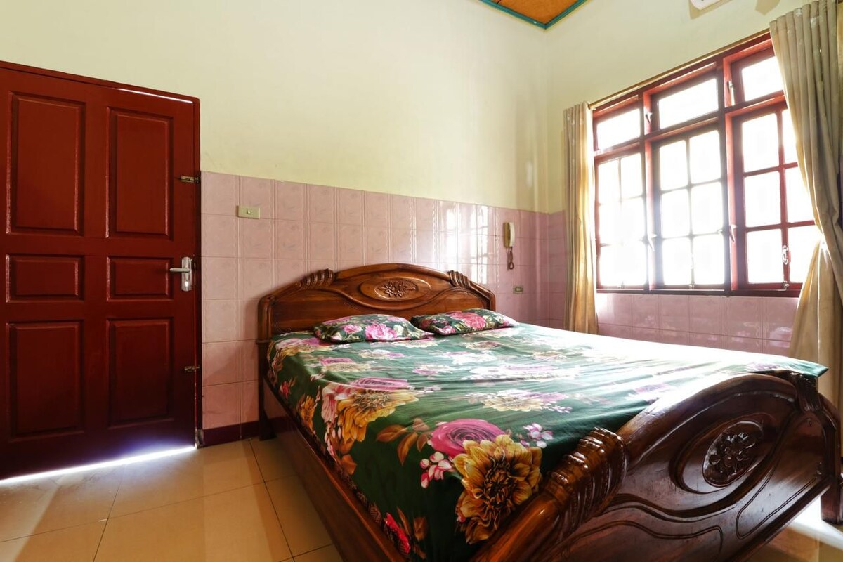 A room with a wooden bed, a red door, and a window with curtains.