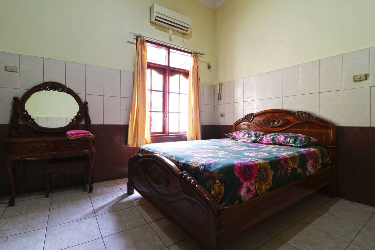 A bedroom with a wooden bed, a wooden dresser, a mirror, and a window with curtains.