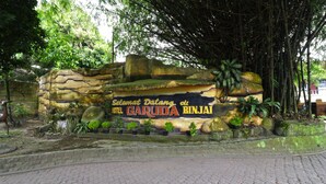 Muro de piedra con un cartel que dice 'Hotel Garuda Binjai', rodeado de follaje.