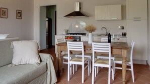 A cozy living room with a sofa and a dining table with chairs. There is a kitchen area with cabinets and a stove. - Agriturismo Villa Borgeri (Castagneto Carducci)