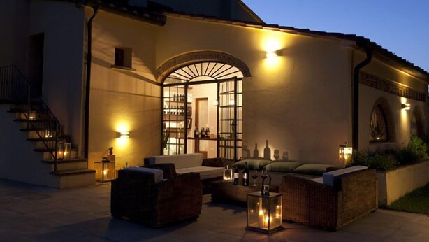 An outdoor seating area with a sofa, chairs, and a table, illuminated by wall-mounted lights. - Agriturismo Villa Borgeri (Castagneto Carducci)