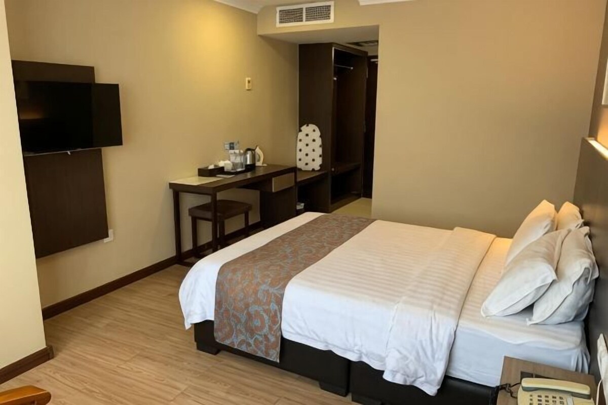 A hotel room with a bed, a desk, a chair, a TV, and a closet.