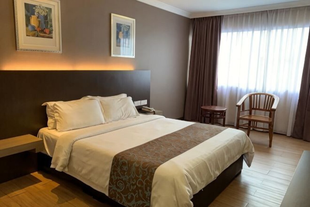 Habitación de hotel con cama, mesita de noche, una silla y ventana con cortinas.