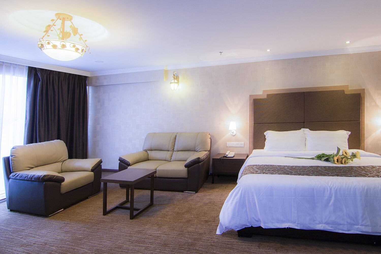 A hotel room with a bed, two sofas, a small table, a nightstand, and a chandelier.