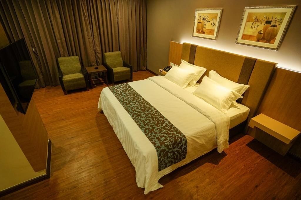 Une chambre d’hôtel avec un grand lit, deux fauteuils, un bureau et une télévision.