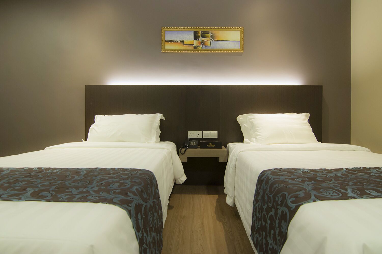 A hotel room with two beds, a nightstand with a phone and a lamp, and a painting on the wall.