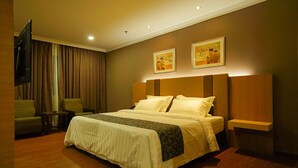 Habitación de hotel con una cama grande, un televisor montado en la pared, una mesita pequeña y dos sillas.