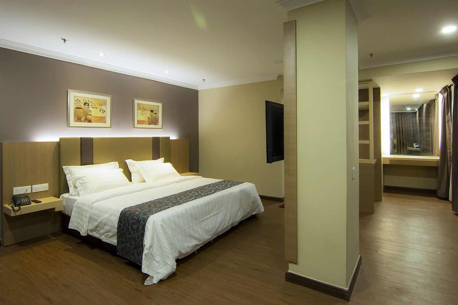A hotel room with a large bed, bedside tables, a flat-screen TV, and artwork on the walls.
