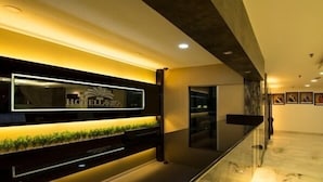 Zona de recepción de hotel con diseño moderno, que incluye un mostrador de recepción, una pantalla digital y una barandilla de cristal.