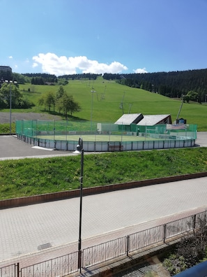 A fenced sports field with a small building, a paved walkway, and a bench.